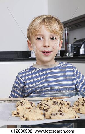 Stock Image - Portrait of happy young boy in front of baking tray of cookies. Fotosearch
