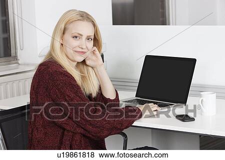 Portrait of happy young businesswoman with laptop sitting at desk in office View Large Photo Image Stock Photo - Portrait of happy young businesswoman with laptop sitting at desk in office. Fotosearch