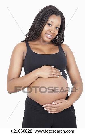 Stock Image - Portrait of happy young pregnant woman with hands on stomach over white background. Fotosearch