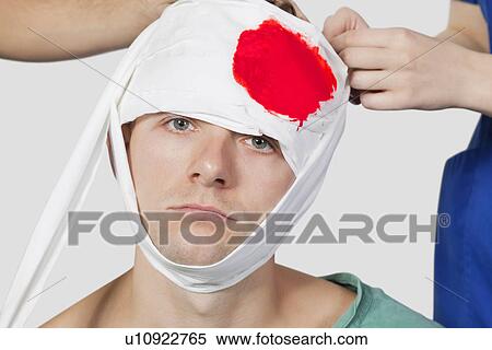Portrait of injured young man being treated by doctors against gray background View Large Photo Image Stock Photography - Portrait of injured young man being treated by doctors against gray background. Fotosearch