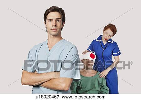 Stock Photo - Portrait of male doctor with female nurse treating an injured patient against gray background. Fotosearch