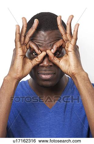 Portrait of playful young man with hands over eyes against white background View Large Photo Image Stock Photograph - Portrait of playful young man with hands over eyes against white background. Fotosearch