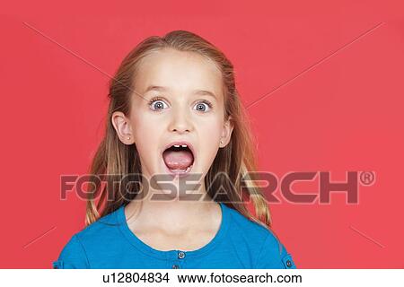 Picture - Portrait of shocked young girl with mouth open against red background. Fotosearch
