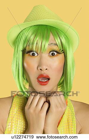 Stock Photo - Portrait of shocked young woman with green hair against yellow background. Fotosearch