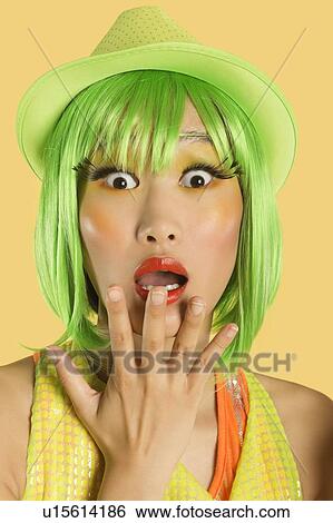 Stock Photograph - Portrait of shocked young woman with green hair against yellow background. Fotosearch