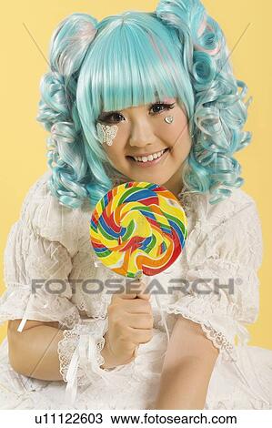 Portrait of smiling young woman dressed as a doll holding lollipop over yellow background View Large Photo Image Stock Image - Portrait of smiling young woman dressed as a doll holding lollipop over yellow background. Fotosearch