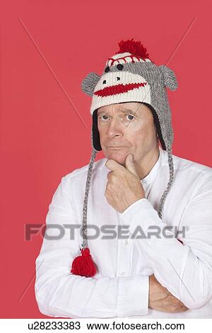 Stock Image - Portrait of thoughtful senior man with hand on chin against red background. Fotosearch