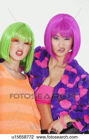 Stock Image - Portrait of two female friends wearing wigs against gray background. Fotosearch