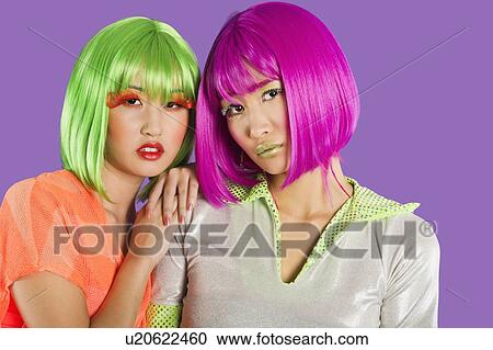 Stock Image - Portrait of two female friends wearing wigs against gray background. Fotosearch