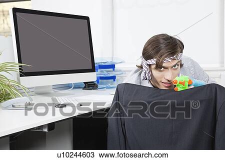 Portrait of young businessman aiming with toy gun at desk View Large Photo Image Stock Image - Portrait of young businessman aiming with toy gun at desk. Fotosearch