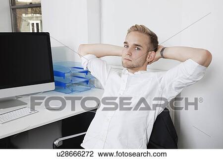 Portrait of young businessman relaxing on chair at office desk View Large Photo Image Stock Image - Portrait of young businessman relaxing on chair at office desk. Fotosearch