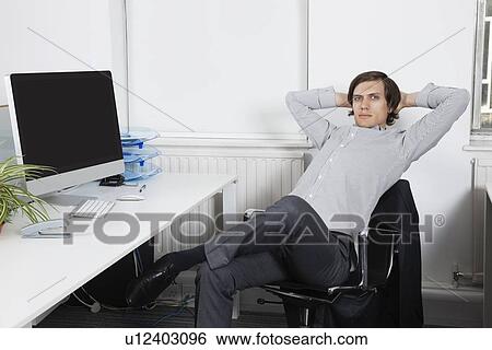 Portrait of young businessman relaxing on chair with hands behind head in office View Large Photo Image Stock Photograph - Portrait of young businessman relaxing on chair with hands behind head in office. Fotosearch