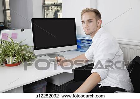 Portrait of young businessman writing notes on paper at desk View Large Photo Image Stock Image - Portrait of young businessman writing notes on paper at desk. Fotosearch