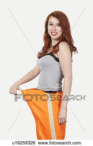 Portrait of young Caucasian woman oversized orange pants against gray background View Large Photo Image Stock Photograph - Portrait of young Caucasian woman oversized orange pants against gray background. Fotosearch