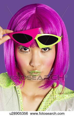 Stock Photograph - Portrait of young funky woman in pink wig puckering lips over purple background. Fotosearch