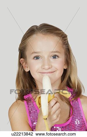Portrait of young girl holding banana against gray background View Large Photo Image Stock Image - Portrait of young girl holding banana against gray background. Fotosearch