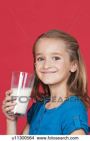 Portrait of young girl holding glass of milk against red background View Large Photo Image Picture - Portrait of young girl holding glass of milk against red background. Fotosearch