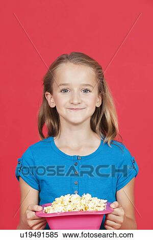 Portrait of young girl holding popcorn container against red background View Large Photo Image Stock Photography - Portrait of young girl holding popcorn container against red background. Fotosearch