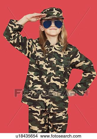 Picture - Portrait of young girl in military uniform saluting against red background. Fotosearch