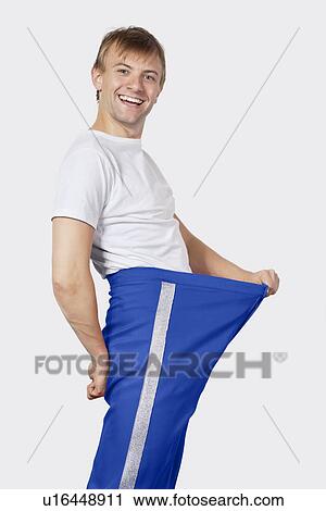 Stock Image - Portrait of young man in oversized blue pants against gray background. Fotosearch