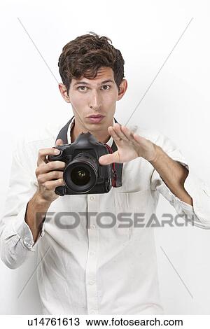 Stock Image - Portrait of young photographer with vintage camera gesturing against white background. Fotosearch