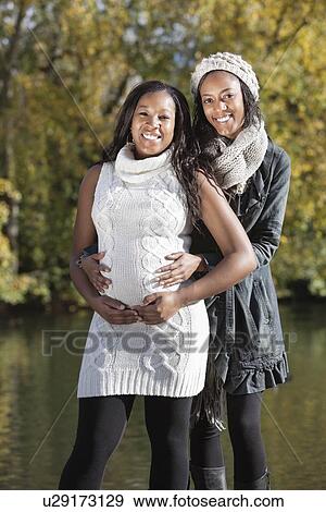 Stock Photo - Portrait of young pregnant woman with female friend spending quality time in park. Fotosearch