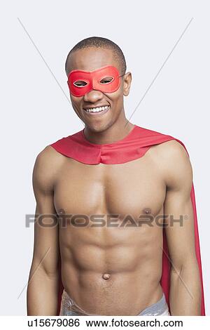 Stock Photograph - Portrait of young shirtless man in superhero costume smiling against gray background. Fotosearch