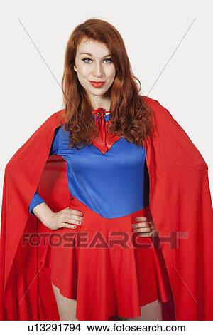 Picture - Portrait of young woman in superhero costume with hands on hips against gray background. Fotosearch