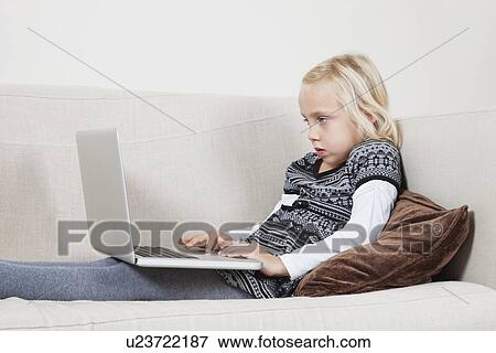 Side view of young girl using laptop on sofa View Large Photo Image Stock Photo - Side view of young girl using laptop on sofa. Fotosearch