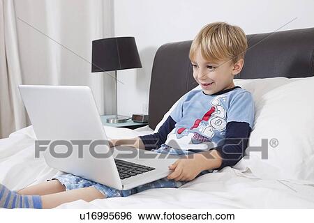 Stock Photograph - Smiling Caucasian boy using laptop computer in bed. Fotosearch