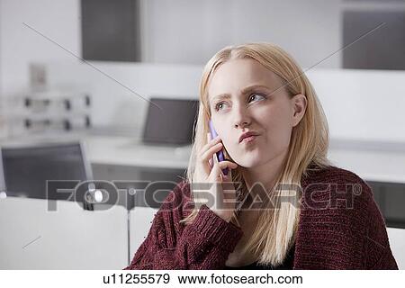 Stock Photo - Thoughtful young businesswoman using cell phone at office. Fotosearch