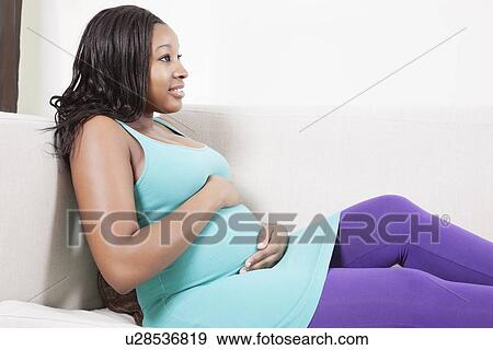 Stock Photo - Thoughtful young pregnant woman relaxing on sofa. Fotosearch
