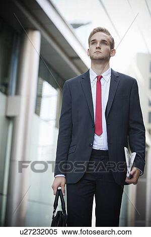 Young businessman in suit holding newspaper and bag View Large Photo Image Stock Photography - Young businessman in suit holding newspaper and bag. Fotosearch