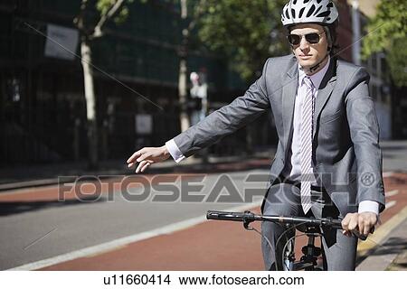 Young businessman showing hand sign while riding bicycle View Large Photo Image Picture - Young businessman showing hand sign while riding bicycle. Fotosearch