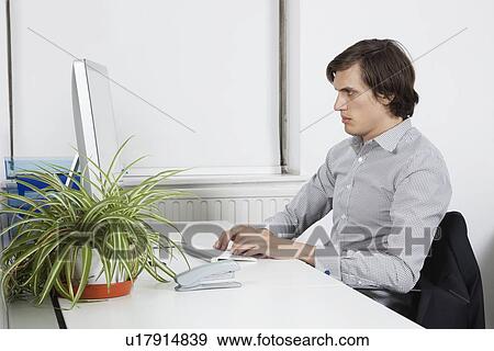 Young businessman typing at office desk View Large Photo Image Stock Photo - Young businessman typing at office desk. Fotosearch