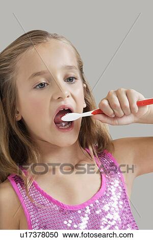 Stock Image - Young girl brushing teeth against gray background. Fotosearch