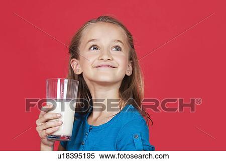 Stock Photography - Young girl holding glass of milk while looking up on red background. Fotosearch