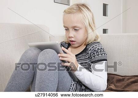 Young girl using digital tablet on sofa View Large Photo Image Stock Photograph - Young girl using digital tablet on sofa. Fotosearch