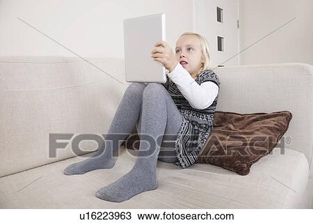 Stock Image - Young girl using tablet PC on sofa. Fotosearch
