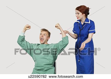 Stock Image - Young male patient with female nurse celebrating success against gray background. Fotosearch