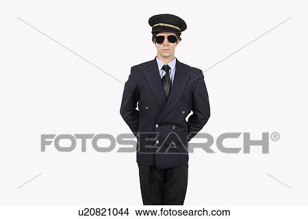 Picture - Young man in pilot uniform standing against gray background. Fotosearch
