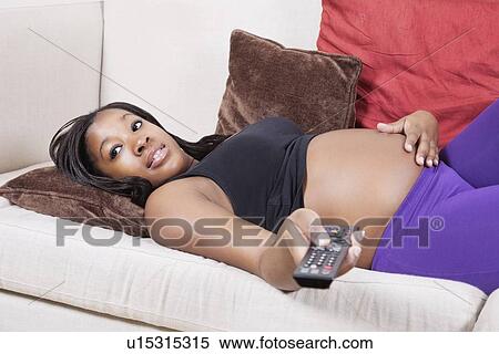 Young pregnant woman watching TV while lying in sofa View Large Photo Image Stock Photography - Young pregnant woman watching TV while lying in sofa. Fotosearch