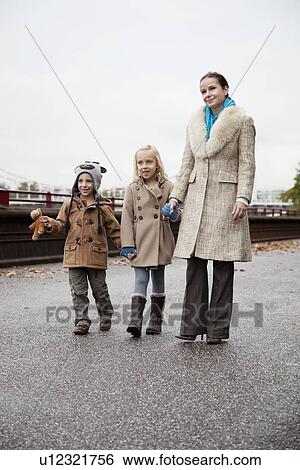 Young woman with children in warm clothing walking together on street View Large Photo Image Stock Photograph - Young woman with children in warm clothing walking together on street. Fotosearch