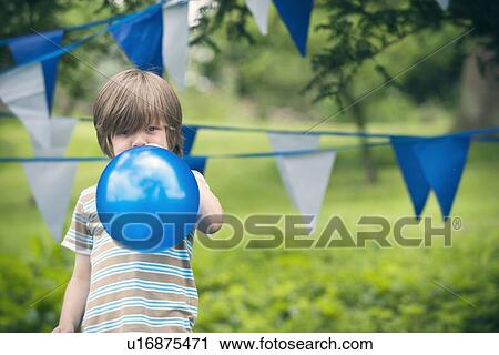Stock Image - Boy blowing up balloon outdoors. Fotosearch