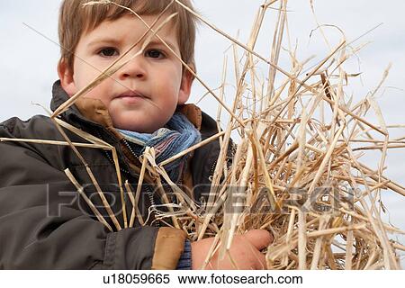 Stock Photography - Boy playing with straw outdoors. Fotosearch