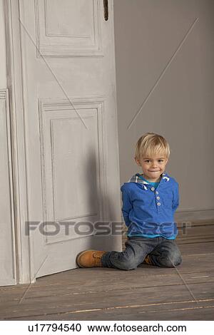 Stock Image - Boy sitting on wooden floor. Fotosearch