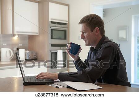 Stock Photography - Businessman working on laptop in kitchen. Fotosearch