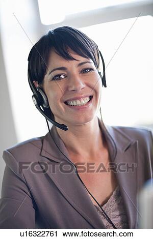 Stock Image - Businesswoman wearing headset at desk. Fotosearch
