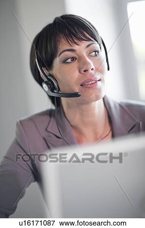 Stock Photo - Businesswoman wearing headset at desk. Fotosearch