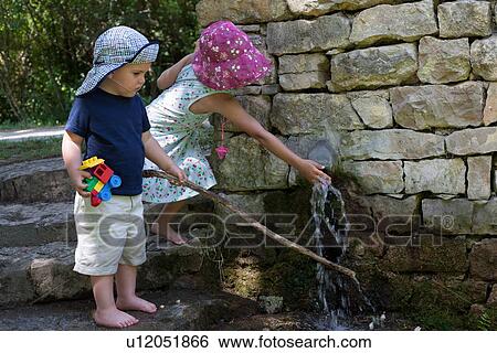 Stock Photograph - Children playing at water spout in wall. Fotosearch
